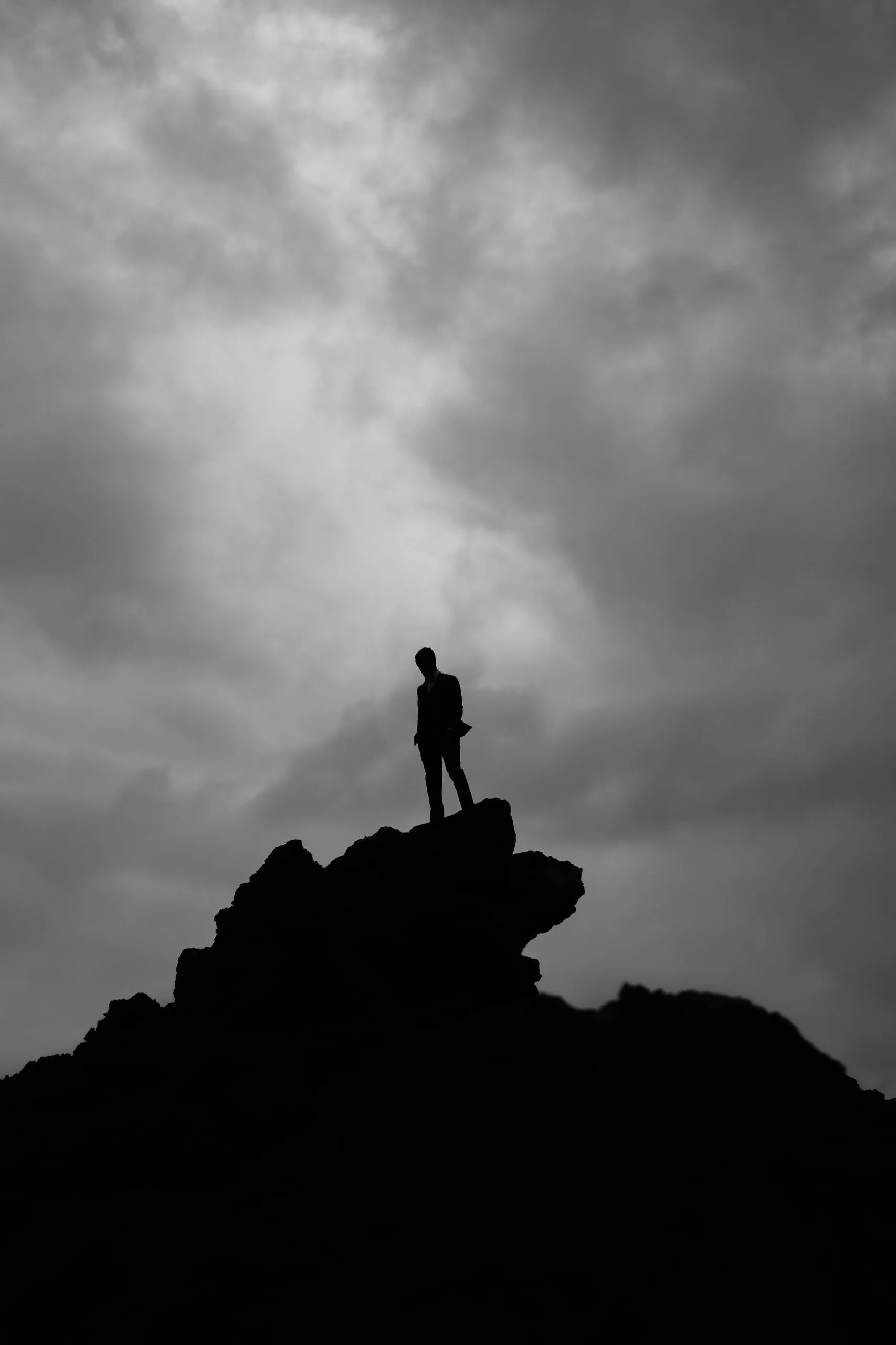 Silhouette des Bräutigams auf einem Felsen vor dramatischem Wolkenhimmel