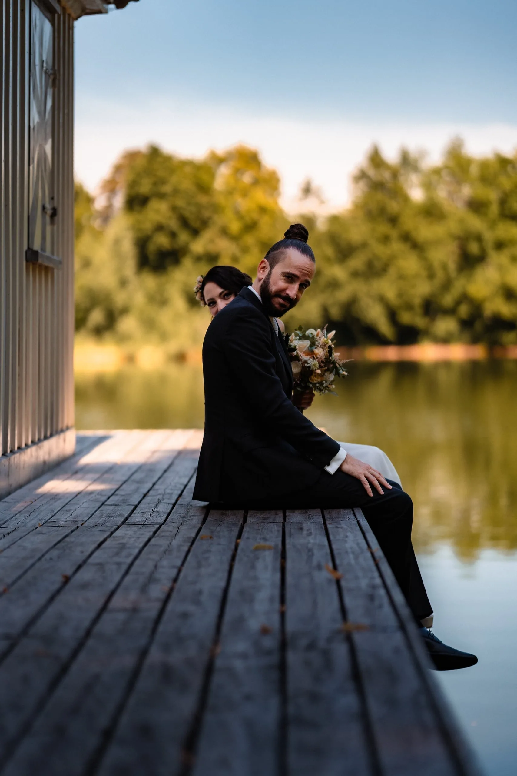Brautpaar sitzt auf dem Bootssteg am See, Braut lugt hervor