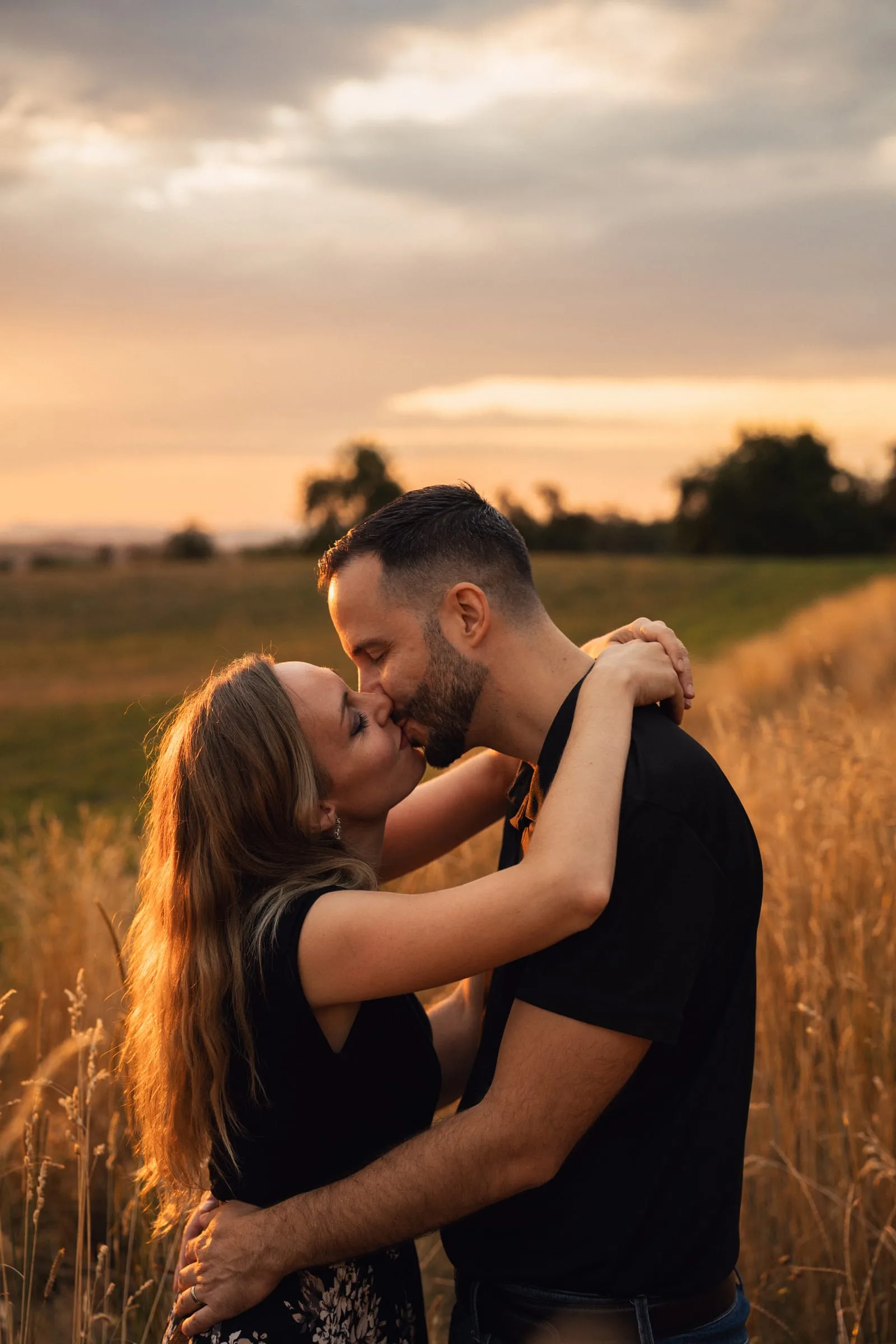 Martina und Stephan küssen sich im hohen Gras, Abendhimmel dahinter