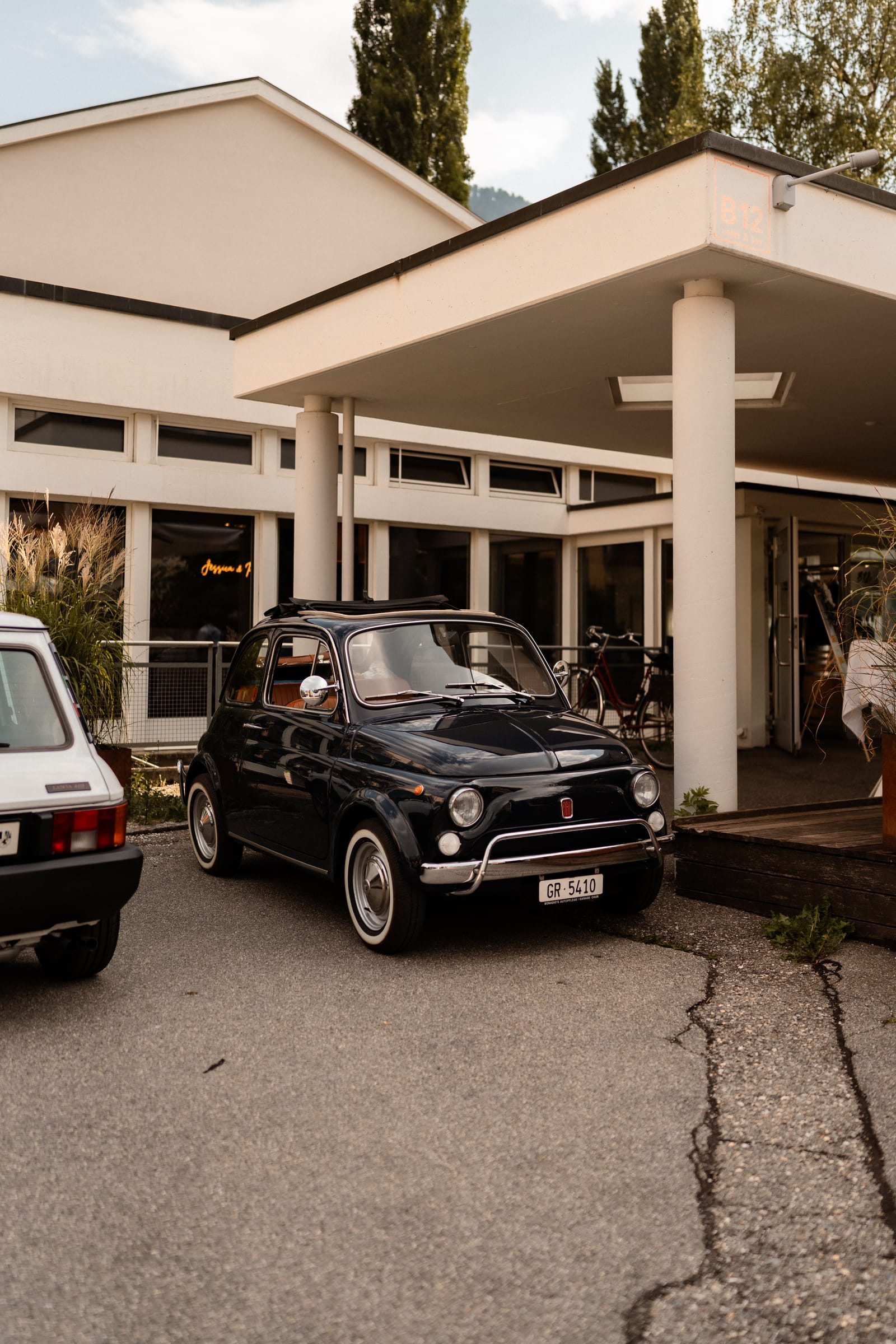 Das modernistische B12-Gebäude in Chur mit weitem Vordach, davor ein dunkler Fiat 500 als Hochzeitsauto