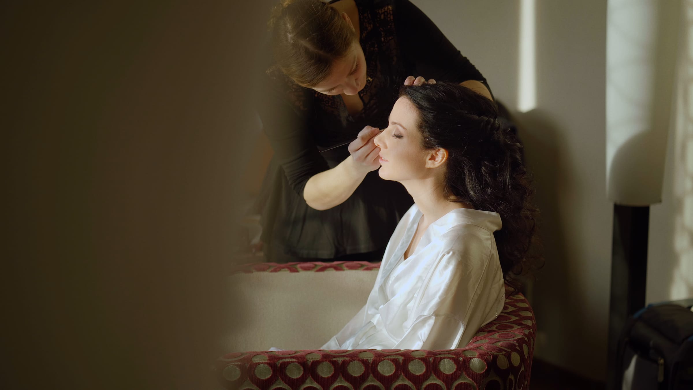 Getting Ready am Hochzeitsmorgen – eine Visagistin schminkt die Braut im warmen Fensterlicht