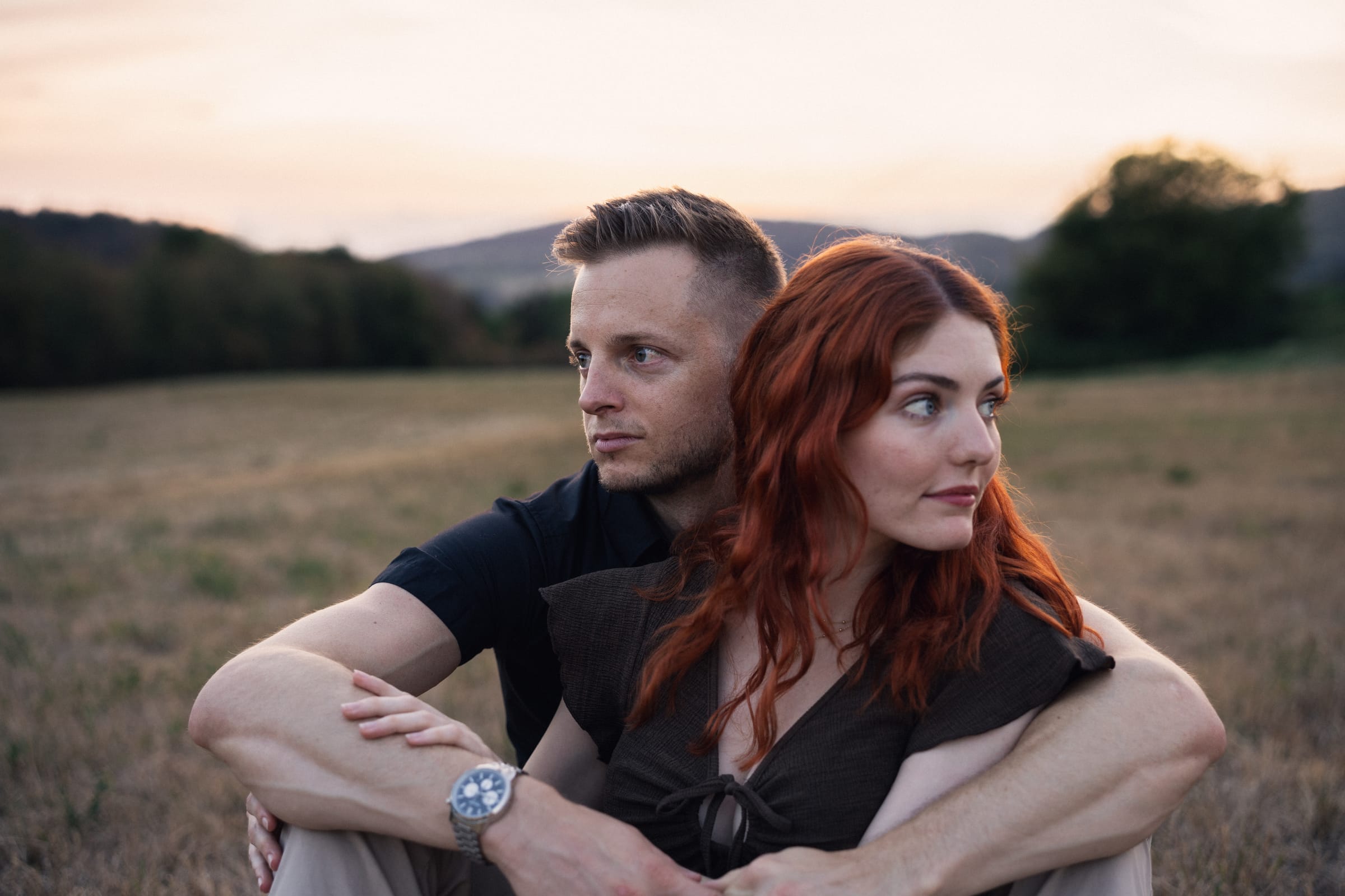 Yanick und Tatjana sitzen eng beieinander auf der Weide, beide blicken zur Seite