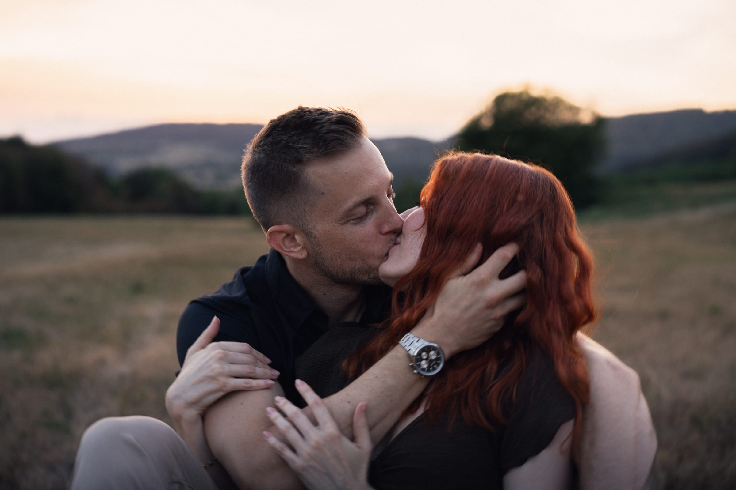 Yanick und Tatjana küssen sich, der Himmel über den Hügeln färbt sich
