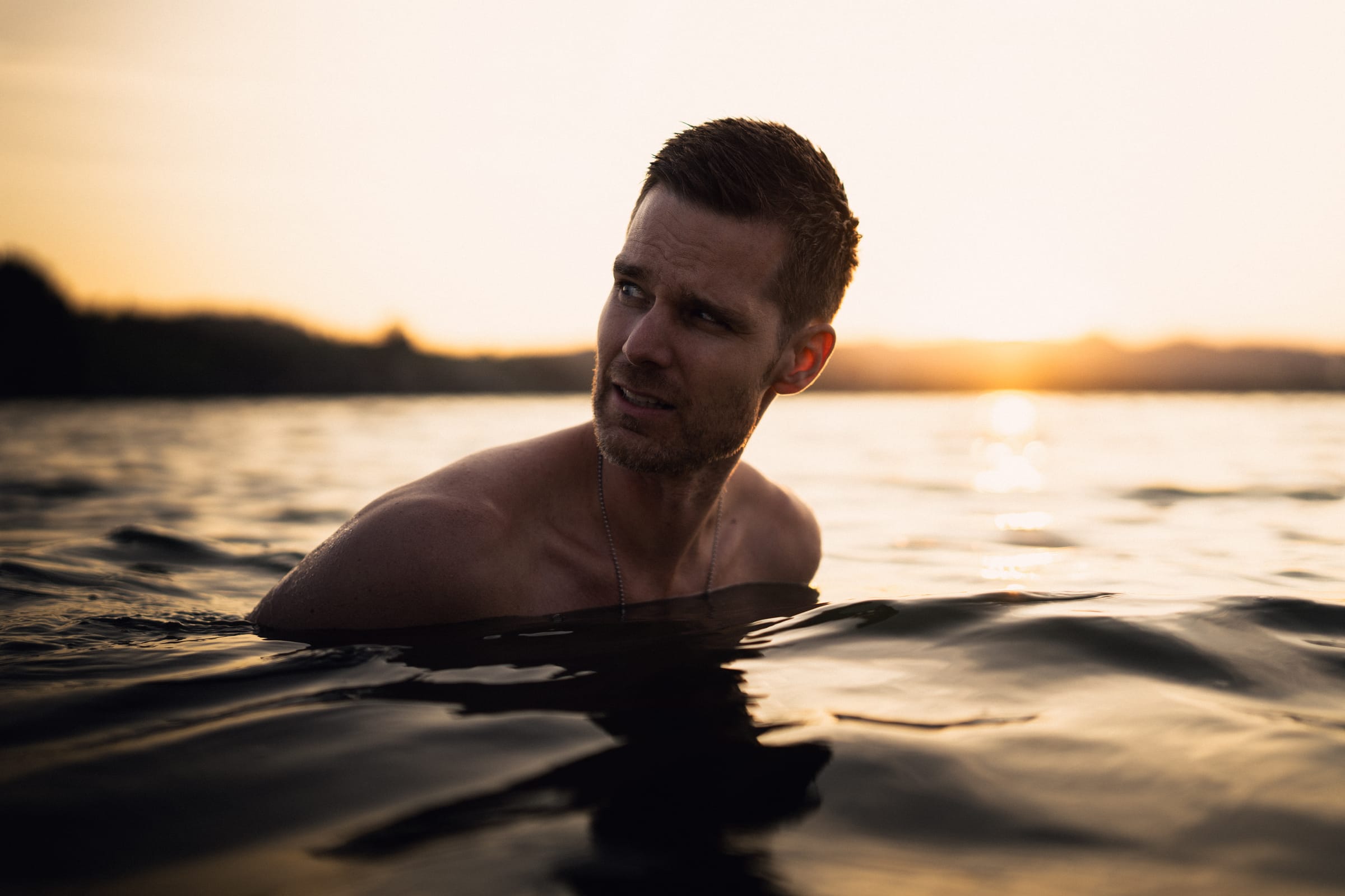 Dani im Wasser des Sihlsees, hinter ihm der Lichtpfad der untergehenden Sonne